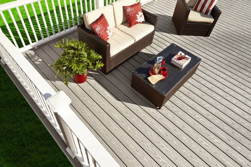 Fiberon Good Life deck with cozy wicker furniture, red accent pillows, and vibrant green lawn.