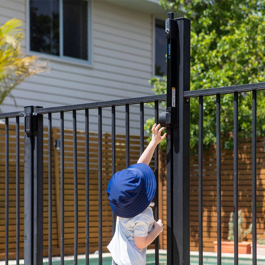 Toddler reaching up toward a top pull MagnaLatch on a black pool fence gate