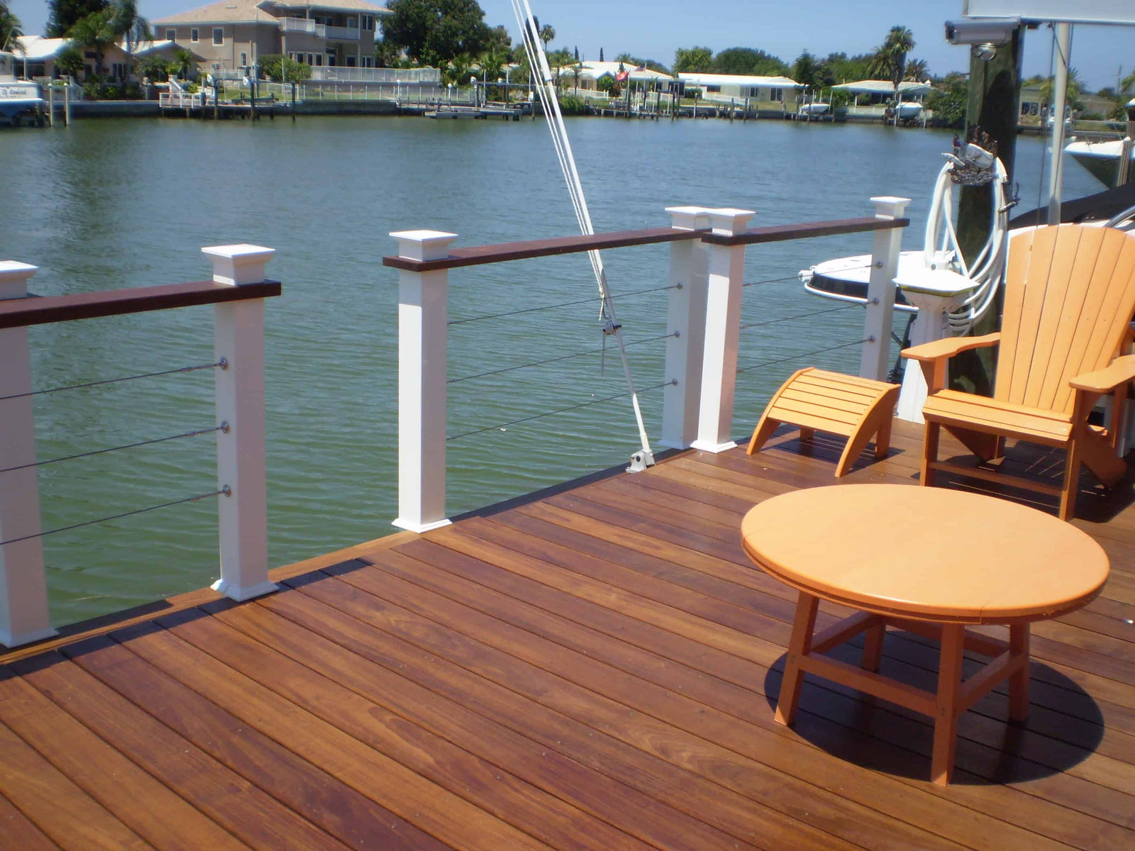 Waterfront deck with cable railing, wooden seating, and an orange Adirondack chair at a Tampa Alvarez Homes project.