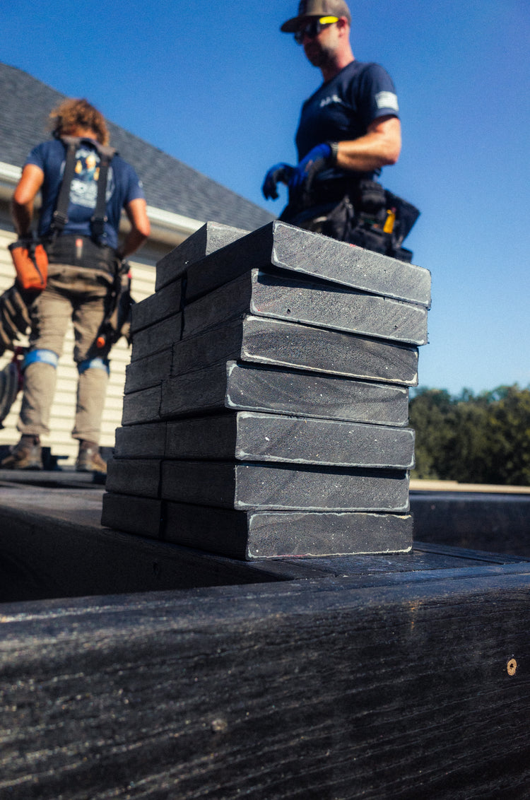 Two workers on a roof with stacks of roofing materials