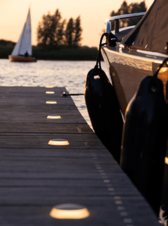 Boat docked at a wooden pier with a sailboat in the background during sunset.