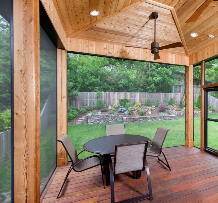 Outdoor patio with wooden ceiling, glass walls, and a round table with chairs.