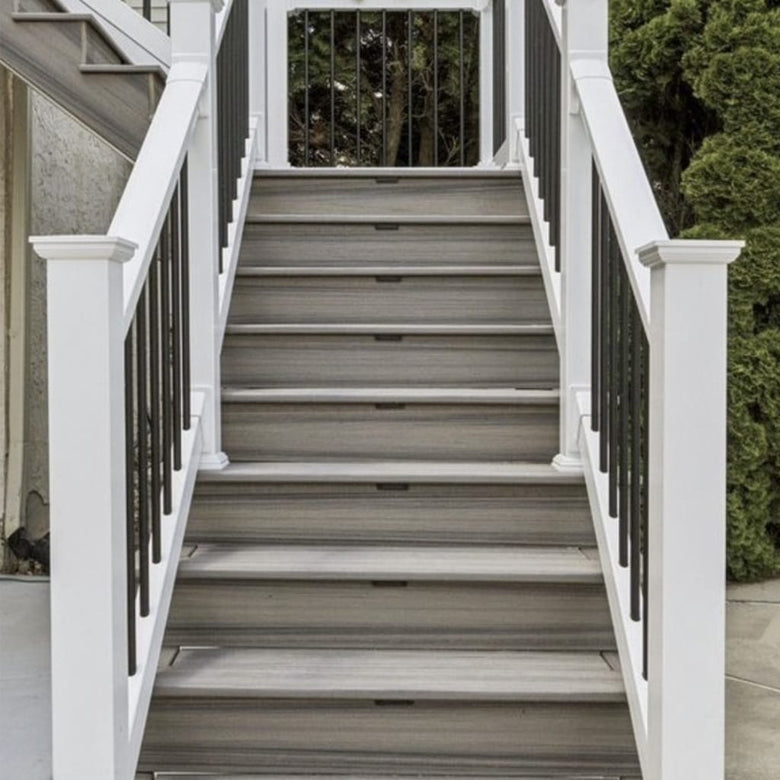Wooden staircase with white railings and black balusters leading to a house.