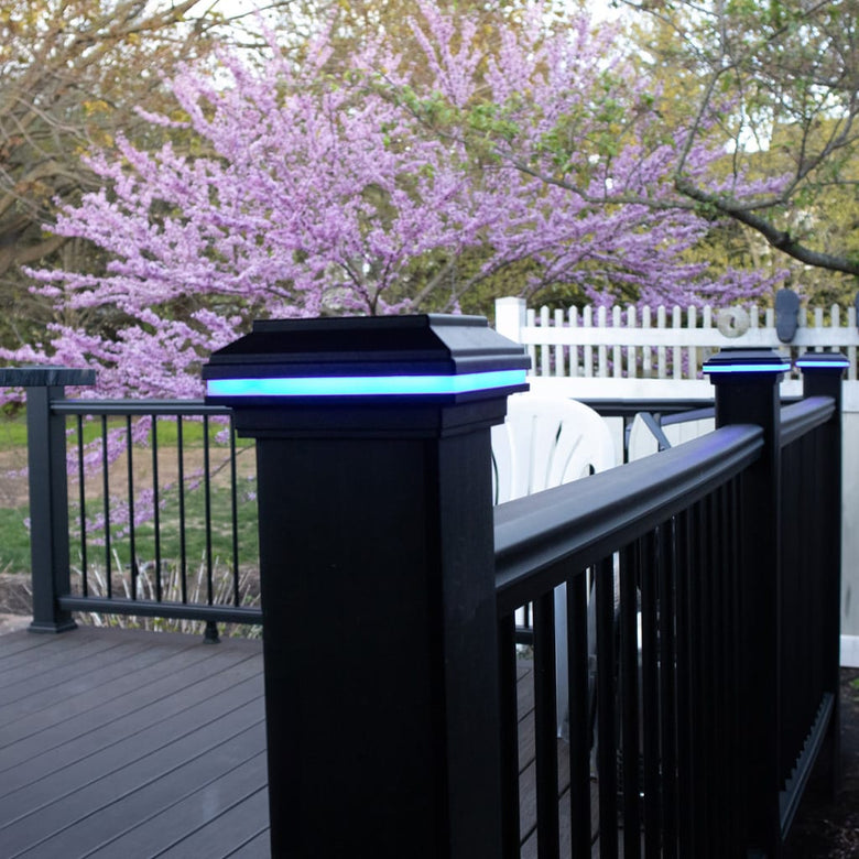 Black railing with solar lights on a deck with a white fence and flowering tree in the background