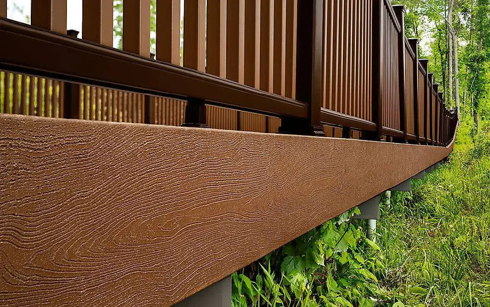 Close-up of Trex fascia board with wood-grain texture beneath brown railing in a lush forest setting.