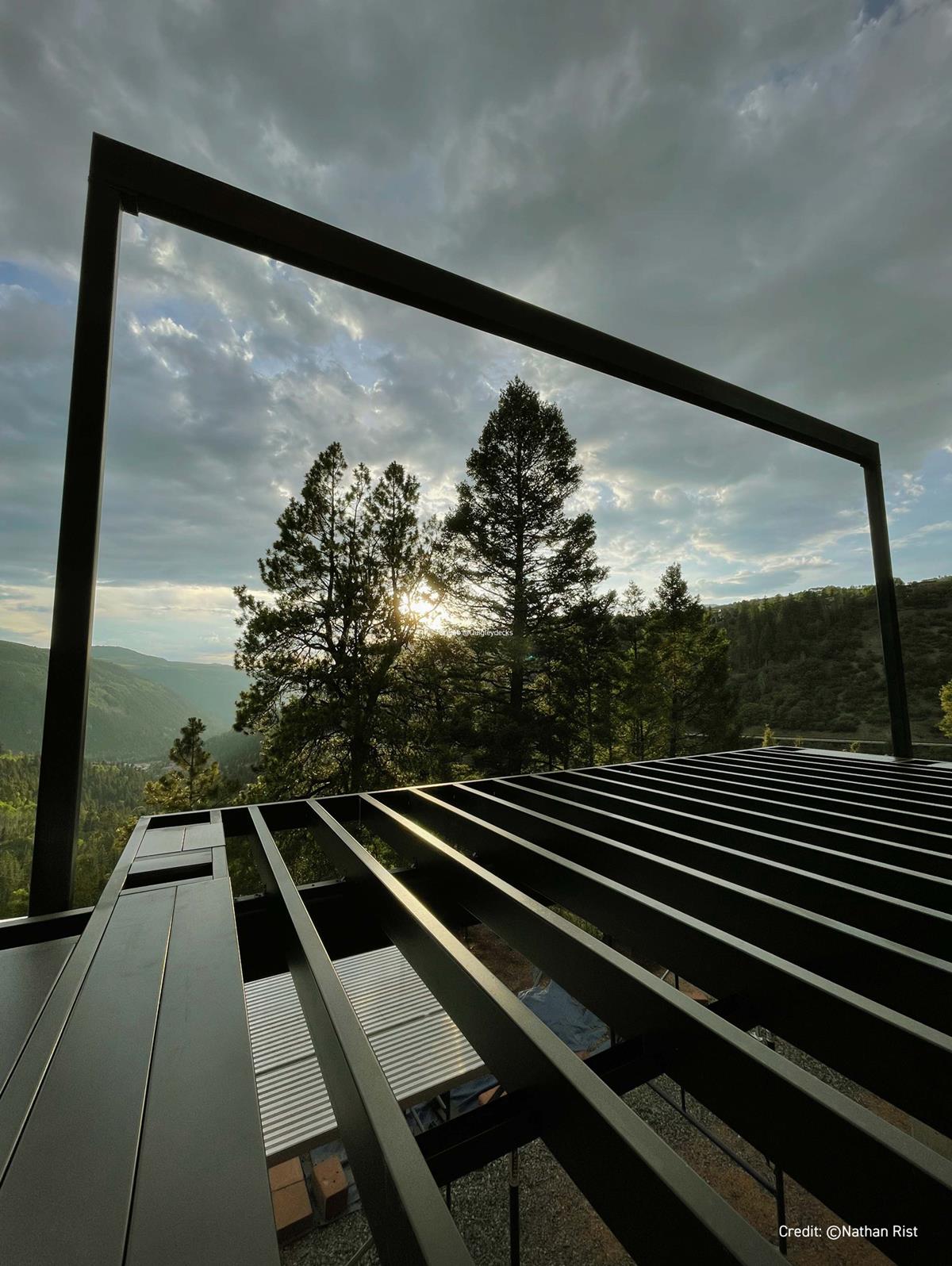 Metal frame structure with a view of trees and mountains under a cloudy sky.