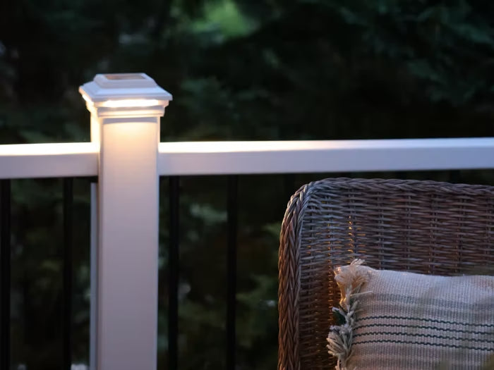 Close-up of a Trex solar post cap light illuminating a deck railing, with a wicker chair and outdoor setting